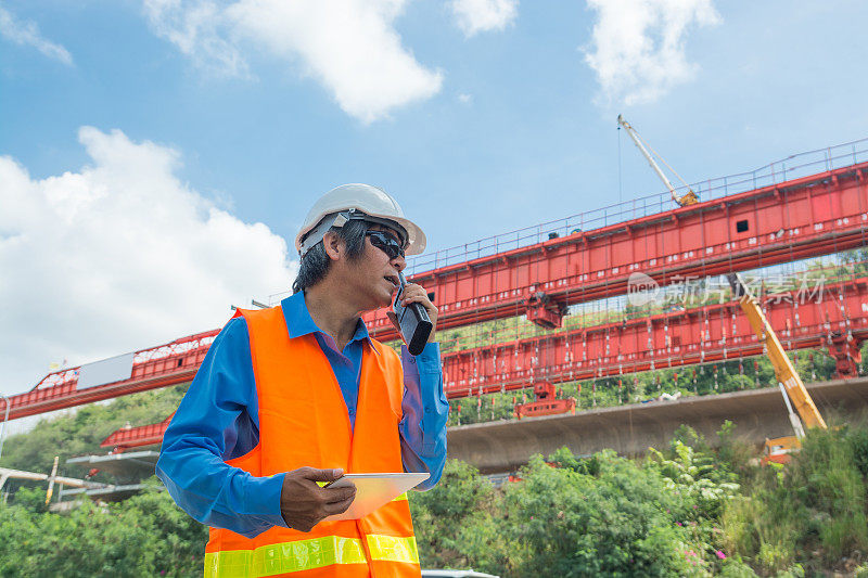 建筑师或工程师，戴白色安全帽和安全背心，使用无线电通讯监督高速公路工程
