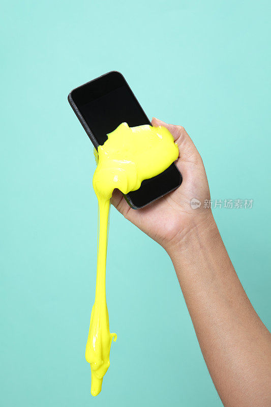 女人的手用智能手机与霓虹灯黄色黏液玩具在绿色波普艺术背景。