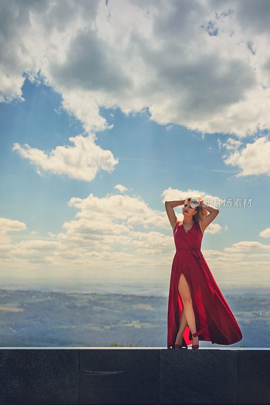 穿着红色长裙的年轻女子在阳光明媚的日子里在山上享受
