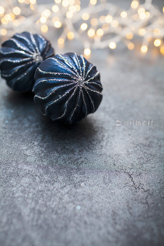 黑色的表面上点缀着蓝色的圣诞装饰物，带有模糊的串灯和复制空间