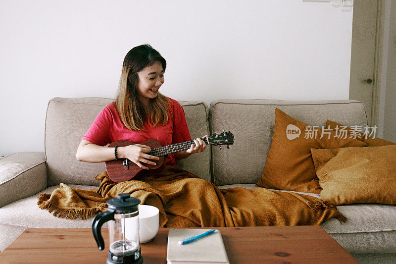 美丽的中国女人在家里弹奏尤克里里