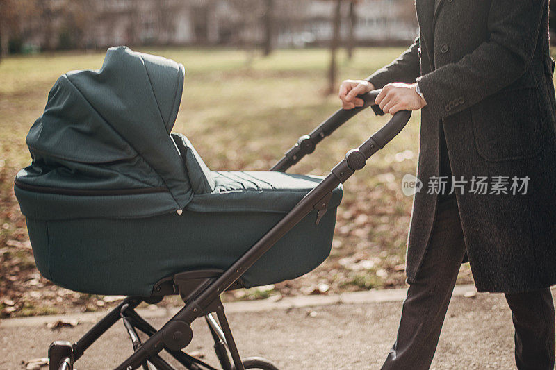 年轻的父亲在公园里推着婴儿车散步