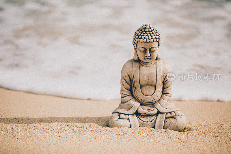 美丽的佛像坐在海边的海滩上，身后是一个即将到来的海浪