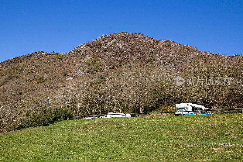 在一个美丽的夏日，威尔士波思马多格附近的威尔士山坡上，一辆大篷车停在阴影中。