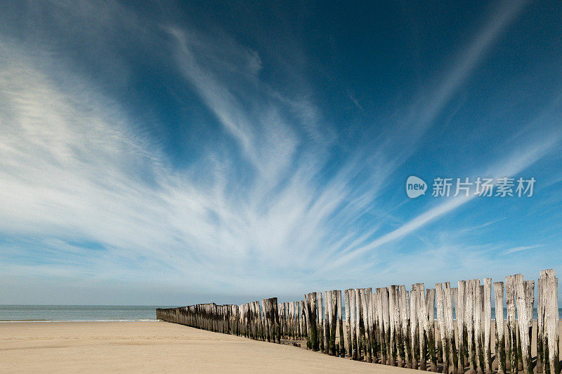 一长排饱经风霜的灰色杆子在海浪中破浪而出。湛蓝的天空，飘着缕缕白云