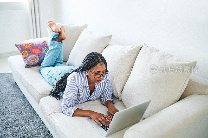 一名年轻女性躺在家里的沙发上使用笔记本电脑