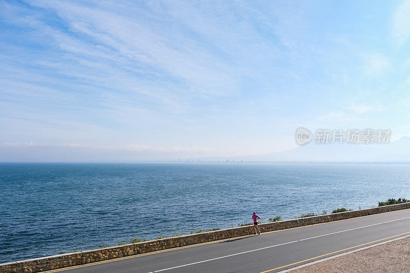 一个女人沿着海边的公路跑步，可以看到海景