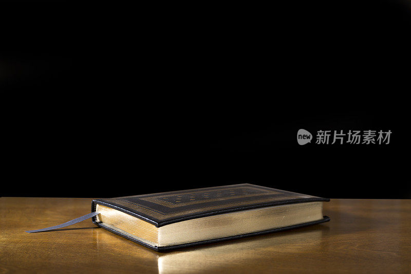 合上的书或圣经放在高度抛光的木桌上。黑色背景。桌子上的书下面有复印的空间。