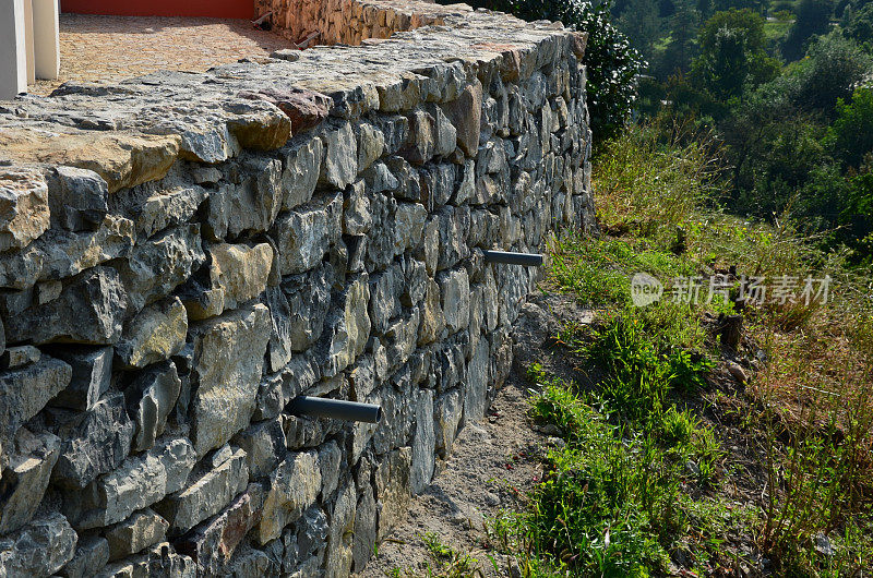 毛石与水泥砂浆结合的漂亮折叠挡土墙。褐色米黄色不规则石灰石。把斜坡保持在上面。排水管离墙。