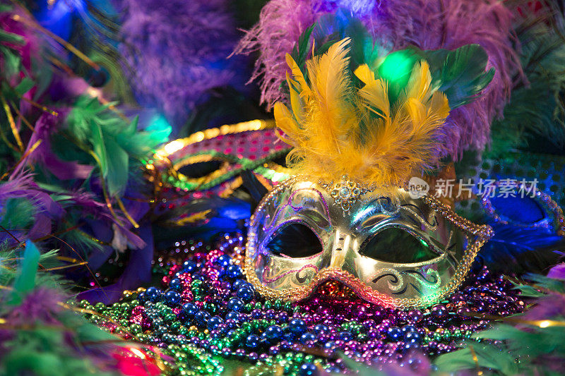 LV狂欢节上的亮片面具，用羽毛装饰在铺有羽毛的床上。彩色的珠子和聚光灯的颜色。
