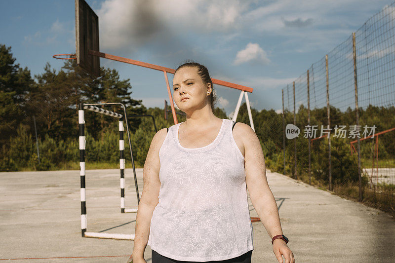 一个超重的女人站在篮球场上，看向别处