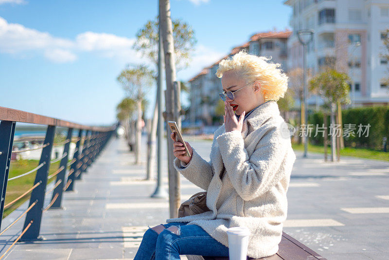 震惊的年轻女子的肖像看着智能手机的屏幕，带着悲伤的表情