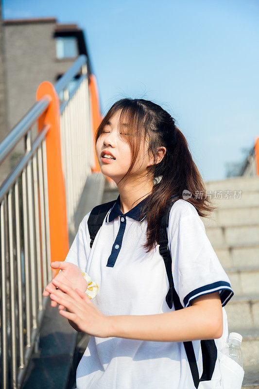 亚洲女孩背着书包在天桥上喝水