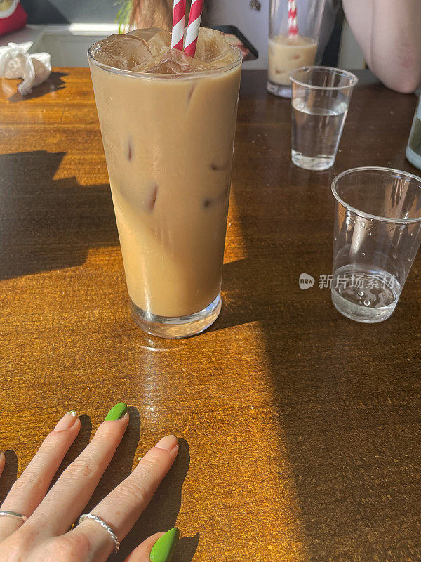 特写图像的手在餐厅桌子上设置与冰块，可生物降解，纸红色和白色条纹饮用吸管，塑料杯的水，油漆钉子和戒指，在背景中无法识别的人，集中在前景