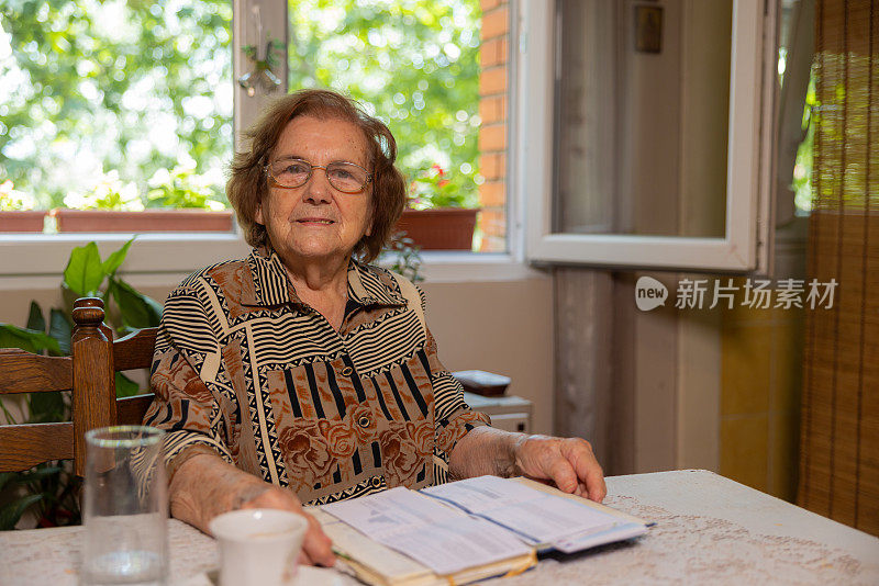 开朗的老年高加索妇女的肖像，94岁，坐在桌子和阅读一本书