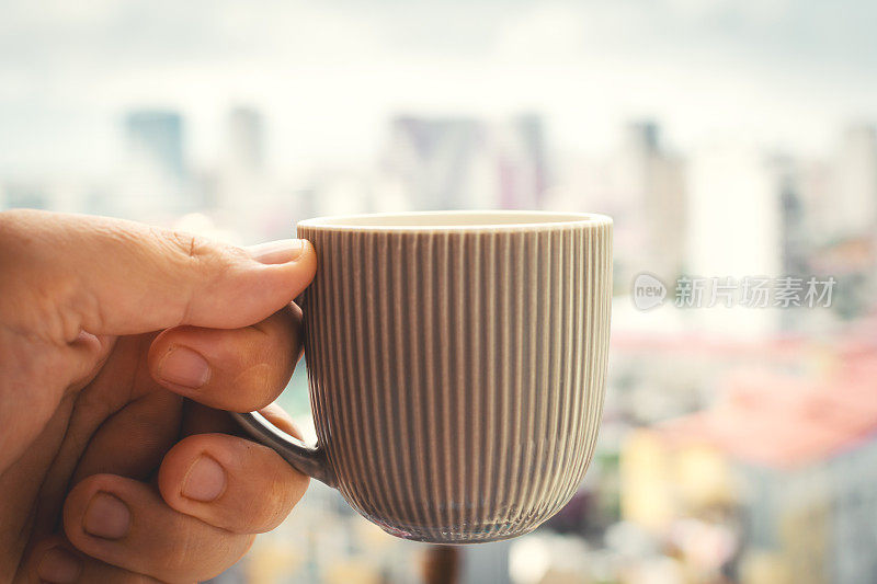 一杯咖啡在手的清晨城市模糊的背景