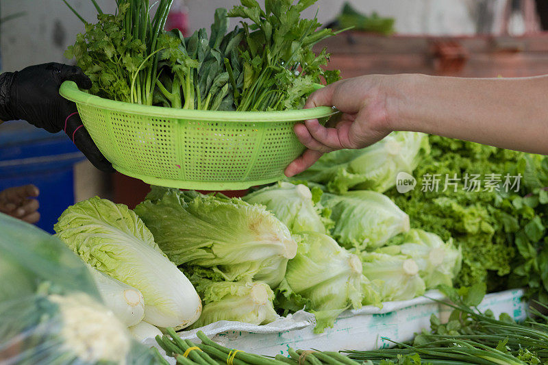 在曼谷当地市场，人的手臂和手伸向蔬菜篮子