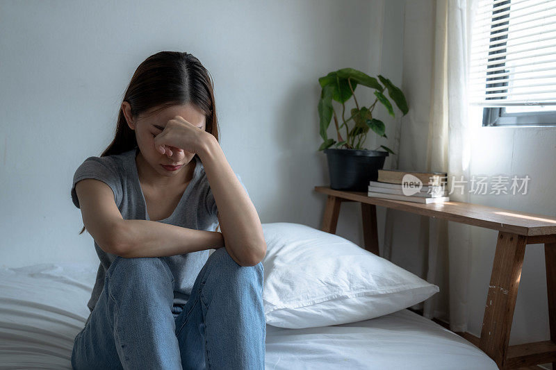 一个亚洲女人独自坐在卧室里，她患有抑郁症，她总是有压力和焦虑。