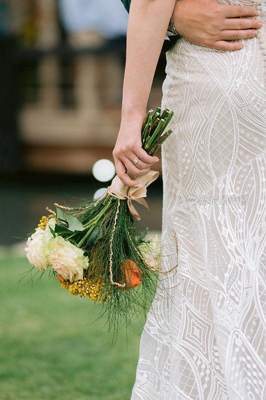 婚礼上新娘的手拿着一束花，新郎的手搂着她的腰
