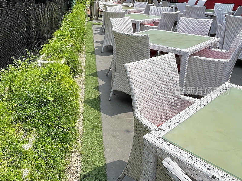 玻璃顶花园露台桌子的特写图像，户外的藤条柳条椅，天井区域的石槽种植芦笋蕨类植物，石板瀑布墙，露天餐厅，重点在前景