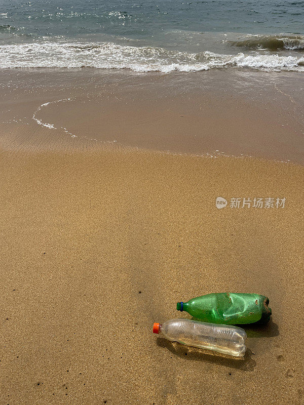 退潮时被冲到沙滩上的两个塑料水瓶，海岸上的海洋垃圾和污染，乱扔的沙子，肮脏的海滩，重点在前景