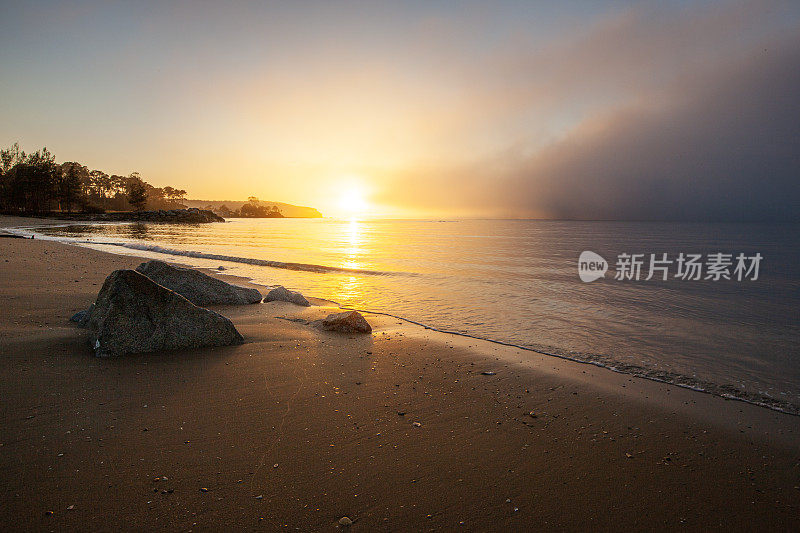 明亮的日出在雾蒙蒙的海面上，海浪拍打着海滩