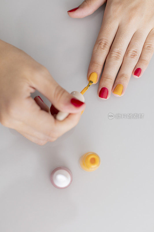 女人用红色和黄色涂指甲。