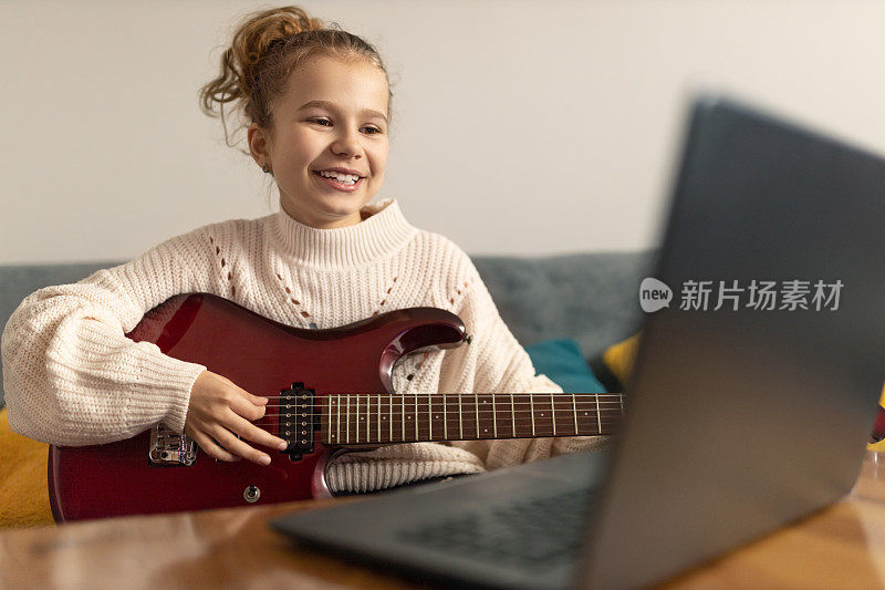 微笑的年轻女孩在家里用笔记本电脑弹电吉他