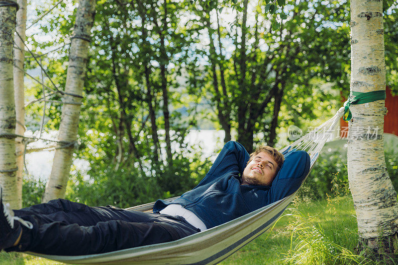 一个快乐的人在夏季挪威森林的吊床上放松