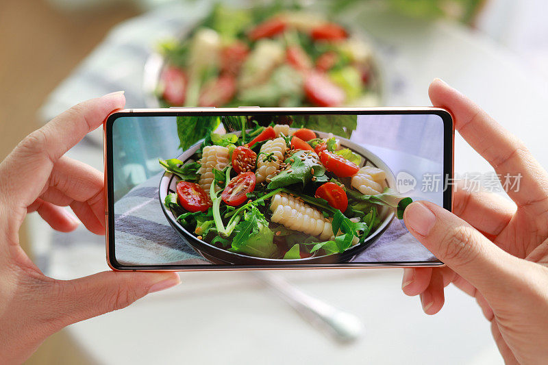 一名亚洲女性用智能手机拍下美味的自制健康沙拉，然后在家里享用。