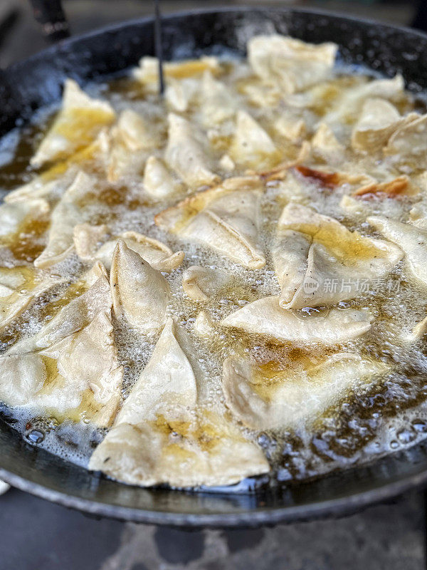 在karahi(印度炒锅)中油炸的一批samosas的特写图像，冒泡的热油，印度街头小吃摊，不健康的饮食，高架视图