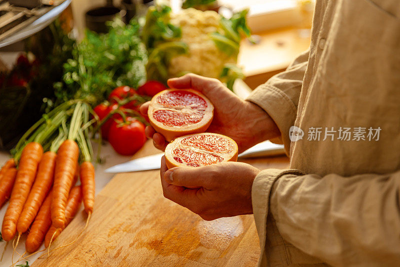 在厨房里，年轻人的手拿着半个红葡萄柚——准备生素食食谱——特写镜头