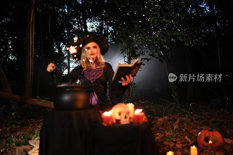 幻想中的女女巫会变魔术，手里拿着一根魔杖和一本魔法书，念着从沸腾的大桶里冒出来的白魔法烟。万圣节的主题。女巫在万圣节那天举行仪式