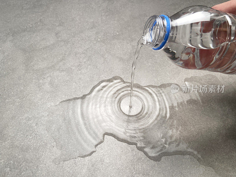 水的概念。一只手把塑料瓶里的水倒在花岗岩瓷砖地板上