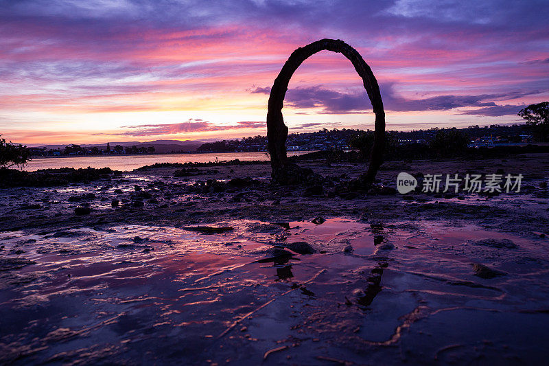 一个美丽的海边日落框在一个铁环反射在一些岩石池的水