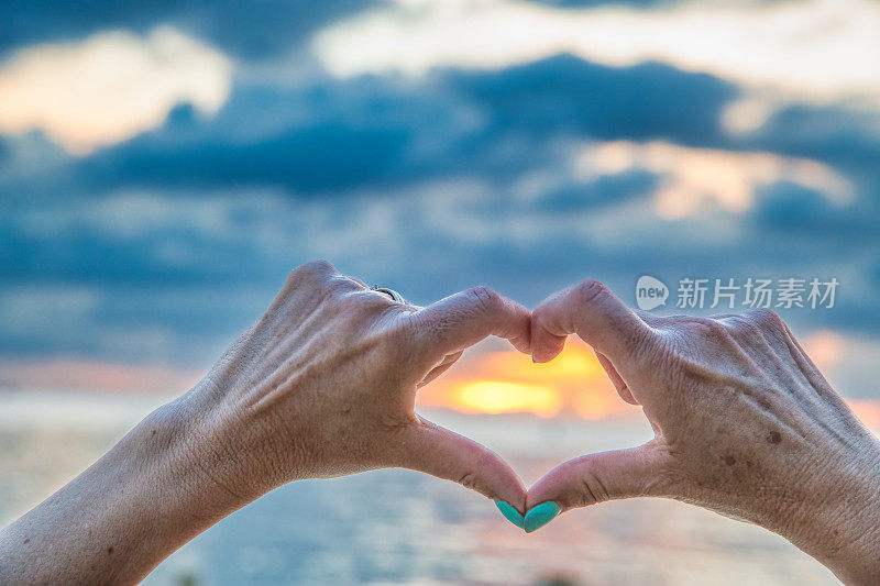 女人在日落与海洋做心形的手