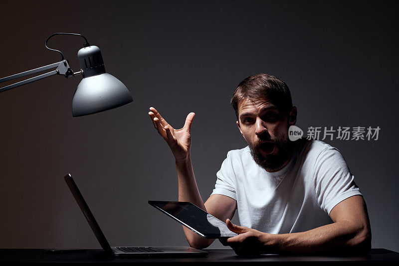 带着笔记本电脑坐在桌子旁的男人深色背景的工作场所办公室情绪灯用手手势模型裁剪视图