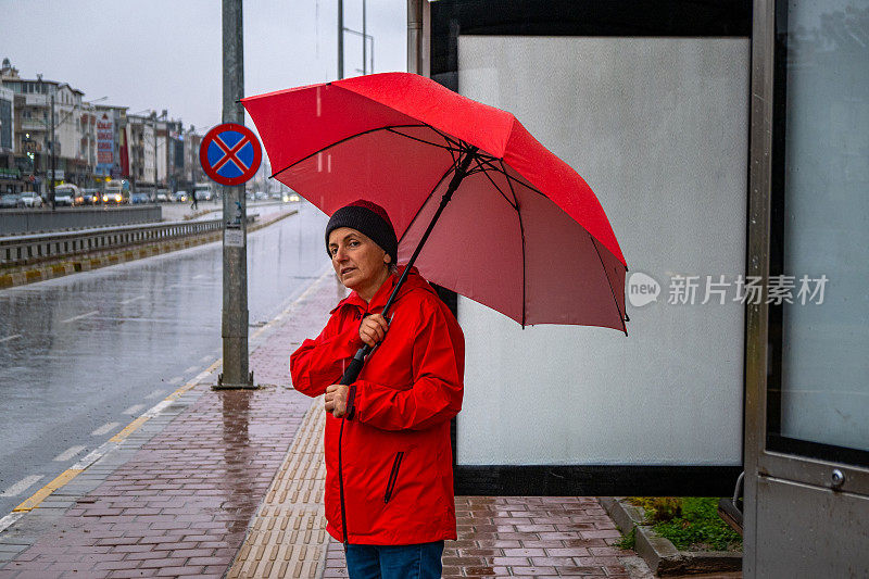 一位女士在雨天撑着伞在公共交通车站等车