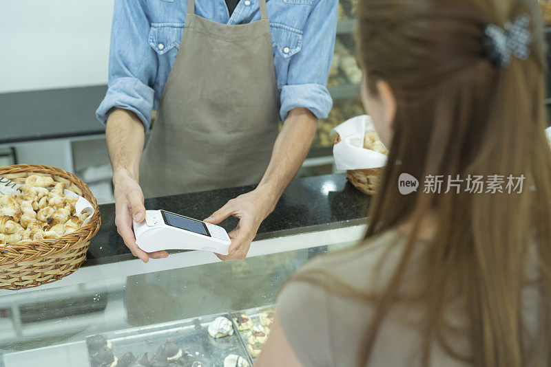 年轻的男面包房员工和女顾客使用终端和智能手表进行非接触式支付