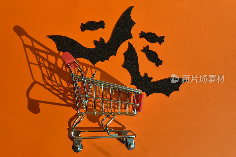 为万圣节做准备。蝙蝠、糖果和橙色背景的毛毡。购物车。秋天。