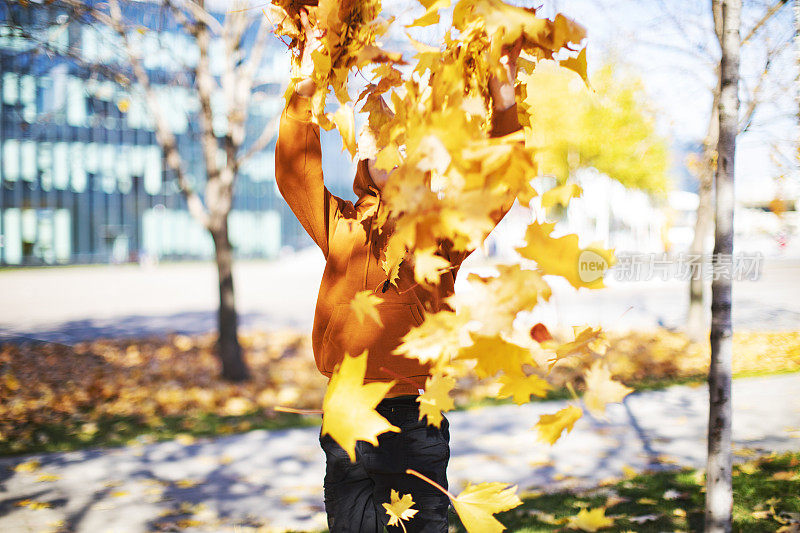 一个孩子在公园里吐着黄色的秋叶