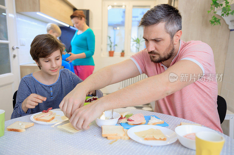 男孩和他的父亲在餐桌上为全家人做早餐三明治