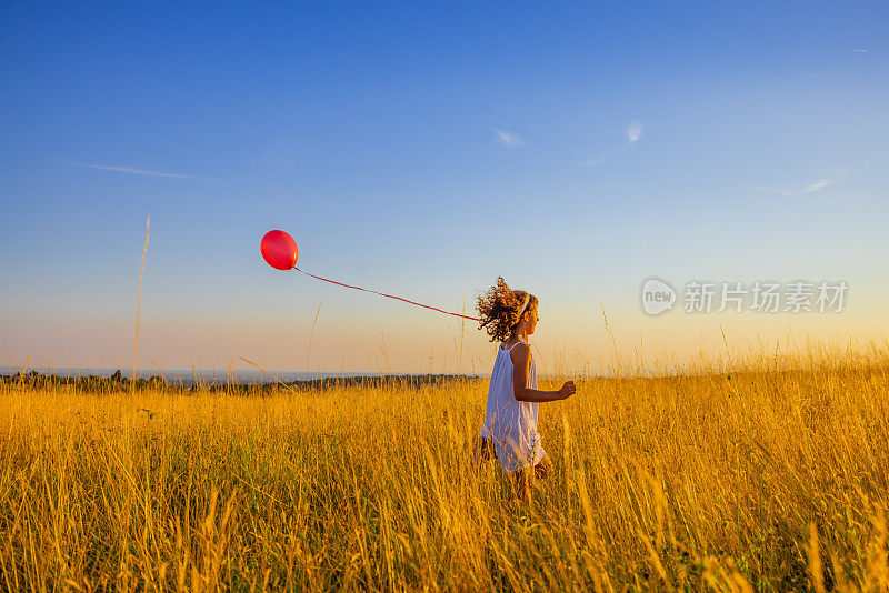 顽皮的女孩与气球奔跑在草地上的草地对天空