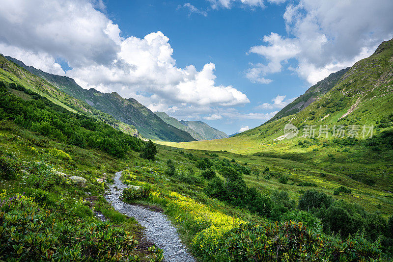 在阳光明媚的日子里，登山驿站在山上，美丽的群山四周被绿色的草和花覆盖着