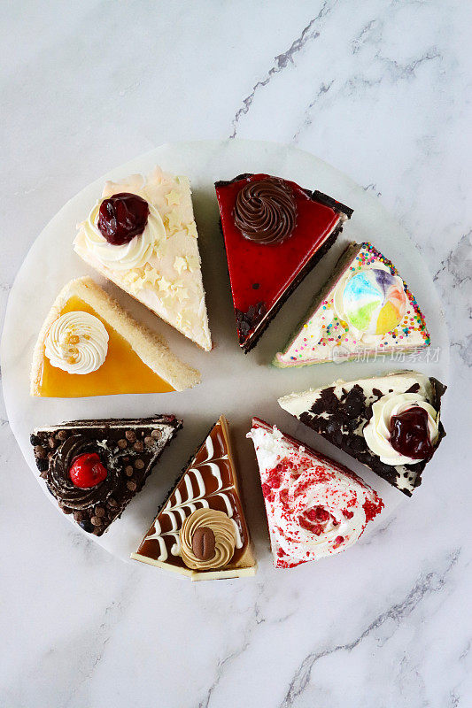 图片上的蛋糕品种切片在圆形的防油羊皮纸，巧克力和樱桃蛋糕，黑森林蛋糕，红色天鹅绒，彩虹蛋糕，咖啡和大理石蛋糕，大理石效果的背景，高架视图