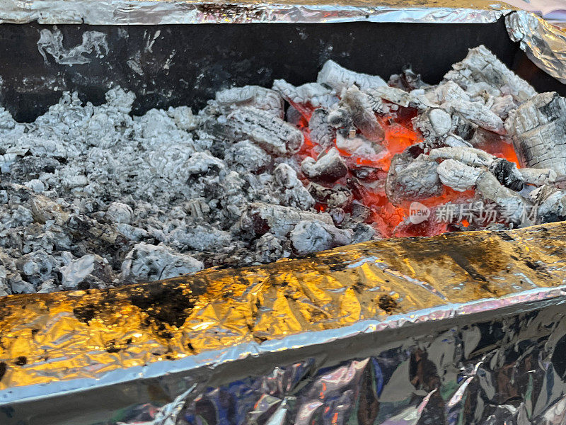 特写图像的金属烧烤托盘充满热木炭余烬和灰烬，火焰带来焦炭加热烹饪，高架视图，重点在前景