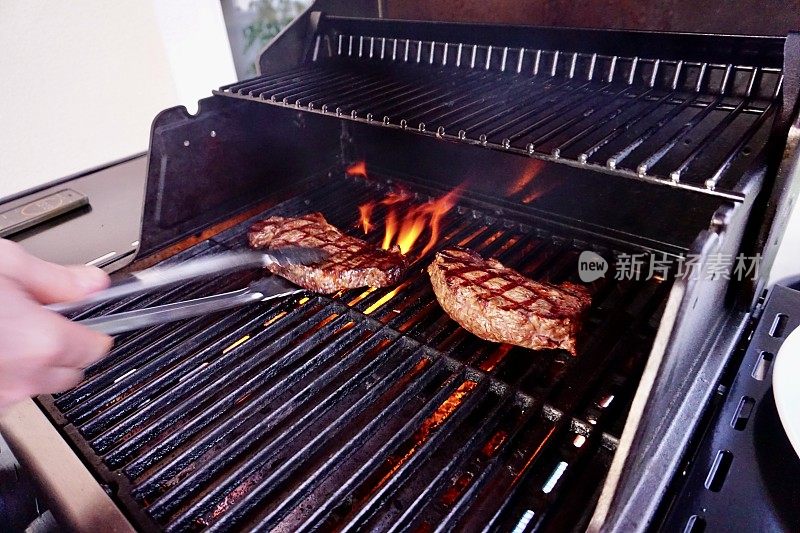 一个男人在烤架上翻牛排。两份烤牛排。火上有两块肉。烤肉和两块肉。烤的肉。