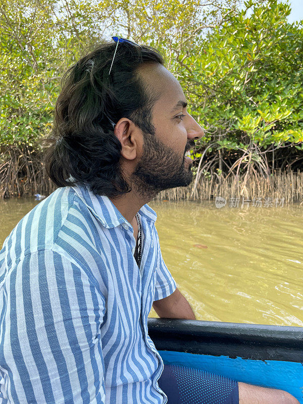 特写图像的印度人坐在渔船船尾与镜像太阳镜在头上，船漂流在泻湖回水浅滩，热带岛屿天堂，侧面视图，重点在前景