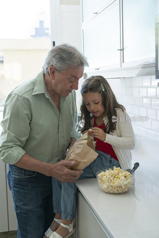 老人和孙女在家里的厨房里吃爆米花，玩得很开心