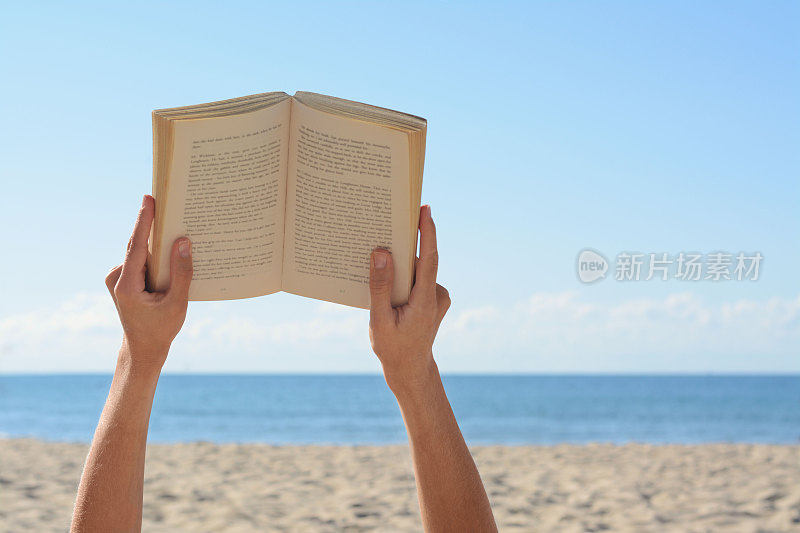 一个女人在海边的沙滩上看书，特写。文本空间